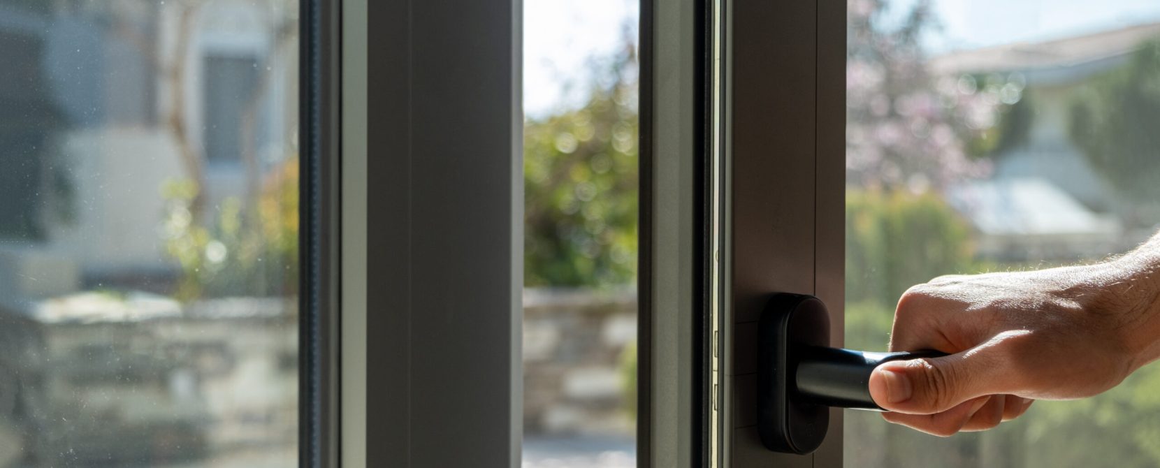 Hand open aluminum window frame closeup view. Man holding the metal or PVC door handle. Energy efficient, security profile, blur garden outdoor background